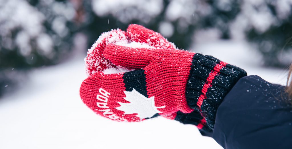 closeup hands red canada mittens make snowball from snow